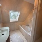 Badezimmer mit Badewanne, Dusche und Fenster mit Blick auf Garten.