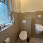 Badezimmer mit Toilette, Wandspüler und Fenster mit Handtüchern.