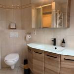 Bad mit Waschtisch, Spiegel und Toilette. Holzschrank und Wandfliesen.