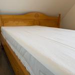Hölzernes Bett mit weißer Matratze in einem Raum mit geneigtem Dach.