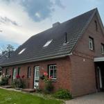 Ein rotes Backsteinhaus mit Dachgauben und Vorgarten. Garage und Blumen sind sichtbar.