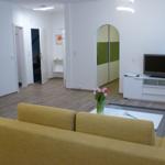 Wohnzimmer mit gelbem Sofa, Fernseher und Holzboden.