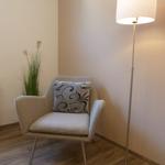 Ein Sessel mit Kissen, eine Stehlampe und eine Pflanze in einem Raum mit Holzboden.