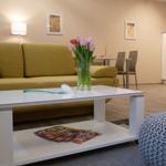 Wohnzimmer mit gelbem Sofa, weißem Couchtisch und Blumen.