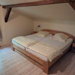 Schlafzimmer mit Doppelbett, Holzboden und Balken. Fenster mit Vorhängen.