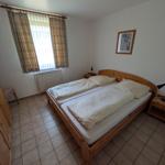 Schlafzimmer mit Doppelbett, Holzbett, Fenster mit Vorhängen und Fliesenboden.
