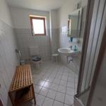 Badezimmer mit Toilette, Waschbecken und Dusche. Holzbank und Fenster sichtbar.