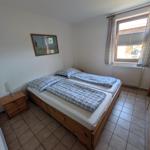 Zimmer mit zwei Einzelbetten, Holzkommode und Fenster mit Jalousie.