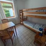Zimmer mit Doppelstockbett, Holztisch und Stühlen, Fenster mit Blick auf Garten.