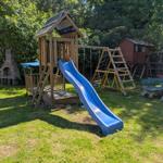 Hinterhof mit Spielplatz, Rutsche und Schaukel. Grasfläche und Bäume im Hintergrund.