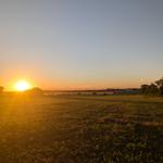 Sonnenuntergang über Feldern mit Windrädern im Hintergrund.