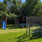 Grüner Garten mit Spielplatz, Tisch, Bank und Fußballtor.