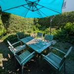Garten mit Holztisch, sechs Stühlen und blauem Sonnenschirm.