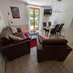 Wohn- und Essbereich mit Sofa, Sessel, Esstisch und TV. Terrasse mit Blick auf Grün.