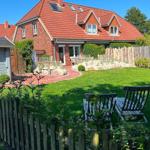 Ein zweistöckiges Haus mit rotem Dach und Garten mit Holzgeländer.