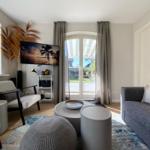 Wohnzimmer mit Sofa, Sessel, Couchtisch und TV. Fenster mit Blick auf Garten.