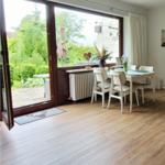 Wohn- und Essbereich mit Sofa, Sessel und Tisch. Durchgang zur Terrasse mit Gartenblick.