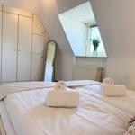 Schlafzimmer mit Dachschrägen, Bett, Kleiderschrank und Fenster mit Blumen.