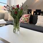 Ein grauer Sofa mit Kissen, ein weißer Tisch und eine Blumenvase.