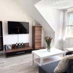 Wohnzimmer mit TV, Couch, Tisch und Fenster. Dachgeschoss mit Holzboden und weißen Wänden.