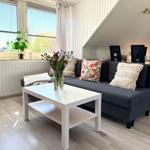 Ein Wohnzimmer mit Sofa, Tisch und Fenster. Im Hintergrund ist ein Esstisch mit Stühlen.
