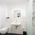 Badezimmer mit Dusche, Waschbecken und Toilette. Weiße Fliesen und Spiegel.
