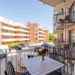 Terrasse mit Tisch und Stühlen. Im Hintergrund mehrstöckige Wohnhäuser und Parkplätze.