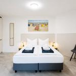 Schlafzimmer mit Doppelbett, Kleiderschrank und Stuhl. Wandbild zeigt Strand.