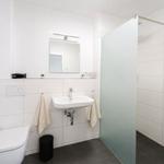 Bad mit Dusche, Waschbecken und Toilette. Weiße Fliesen und dunkle Bodenfliesen.