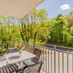 Terrasse mit Tisch und Stühlen, Blick auf grüne Bäume und Straße.