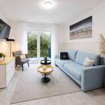 Wohnzimmer mit Sofa, Couchtisch und TV. Balkon mit Blick auf Grün.
