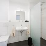 Bathroom with shower, sink, and toilet. White tiles and gray floor.