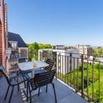 Terrace with table and chairs. View of residential buildings and green areas. Clear blue sky.