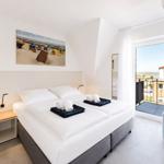 Bedroom with double bed, balcony, and wall art of beach chairs.