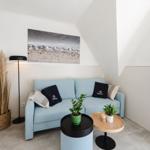 Ein Wohnbereich mit einem hellblauen Sofa, zwei Tischen und einer Wanddekoration.