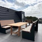 Terrasse mit Holztisch und Bänken, Blick auf Dächer und Landschaft.