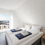 Zimmer mit Doppelbett, Balkon und Nachttisch mit Pflanze.