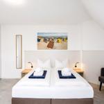 Schlafzimmer mit Doppelbett, Wandbild und Sitzgelegenheit.