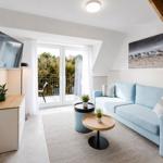 Wohnzimmer mit blauem Sofa, TV und Balkon. Holztreppe und Wandbild sichtbar.
