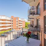 Balcony with table and flowers, view of apartment building and parking lot.