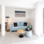 Ein Wohnzimmer mit blauem Sofa, zwei runden Tischen und einer Glastür zum Balkon.