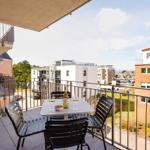 Balcony with table, chairs, and wine bottle. View of modern buildings and green areas.
