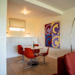Essbereich mit runden Tisch, roten Stühlen und Wandbild. Sofa und Boden sind rot.