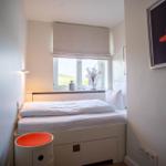 Schlafzimmer mit weißem Bett, Fenster und Kunstwerk an der Wand.