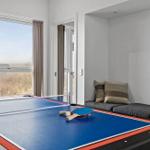 Tischtennis-Tisch mit Schlägern und Ball. Fenster und Sitzgelegenheit im Hintergrund.
