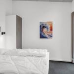 Schlafzimmer mit weißem Bett, Wandbild und Fenster zur Terrasse.