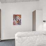 Schlafzimmer mit weißem Bett, Wandbild und Glastür zum Balkon.