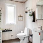 Badezimmer mit Toilette, Waschbecken und Fenster. Holzwände und Pflanzen.