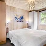 Schlafzimmer mit Holzwand, Bett, Kleiderschrank und Fenster mit Blick auf Bäume.