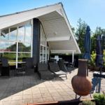Terrasse mit Sitzgelegenheiten und Grillplatz. Hintergrund: Wald und Haus mit Glasfassade.